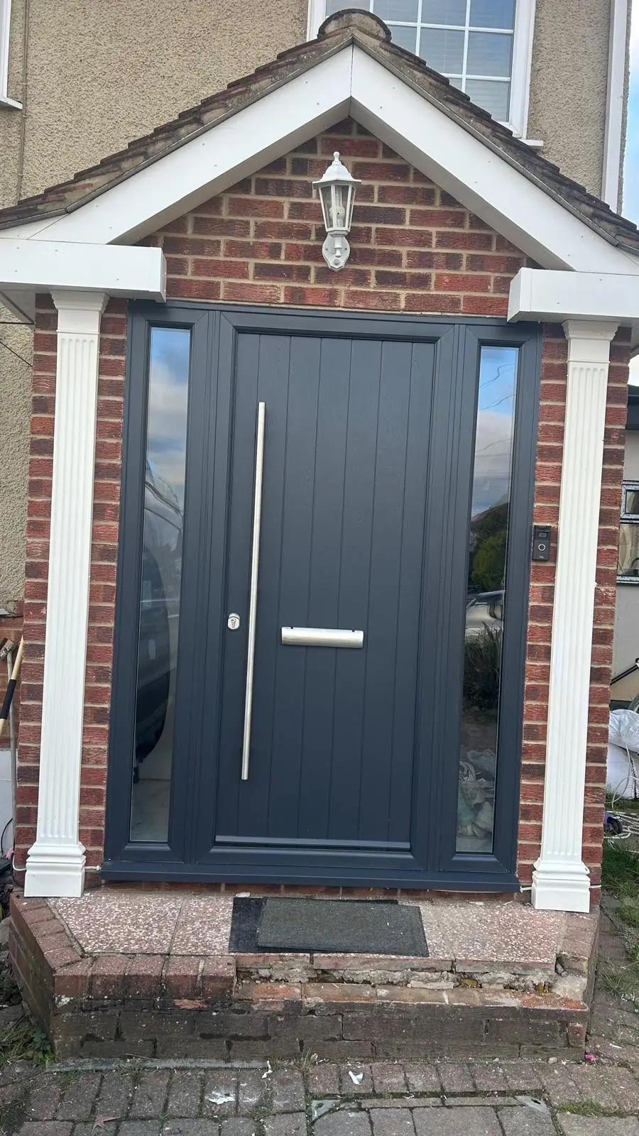 Grey composite front door with sidelights in a brick porch